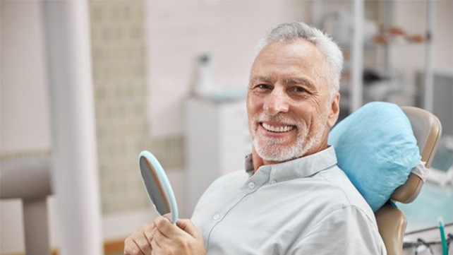 Smiling senior man in dental chair holding a mirror