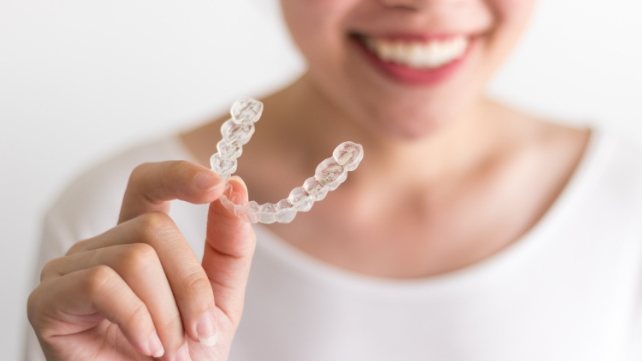 Smiling person holding an Invisalign clear aligner in Colchester