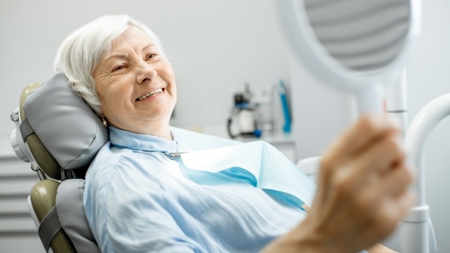 Senior woman looking at smile in mirror after denture placement
