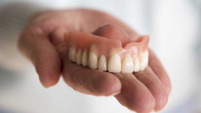 Hand holding denture after caring for dental restoration