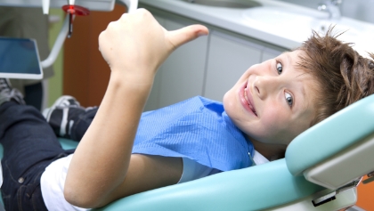 Child giving thumbs up after receiving fluoride supplements in dental chair