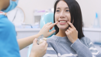 Woman in dental chair pointing to her smile