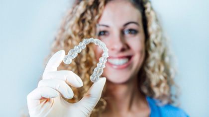 Smiling dental hygienist holding up an Invisalign aligner