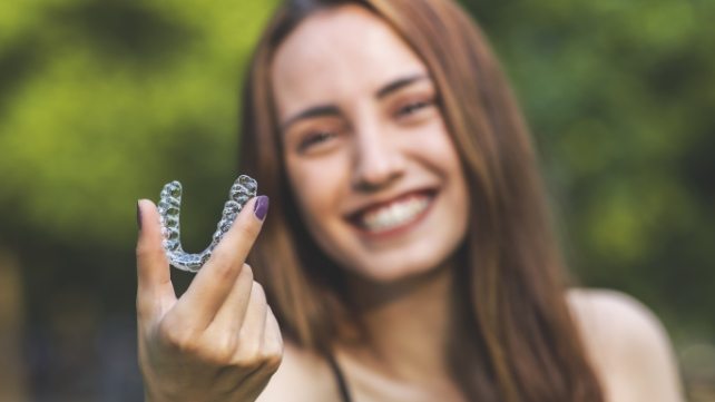 Smiling young woman holding an Invisalign tray