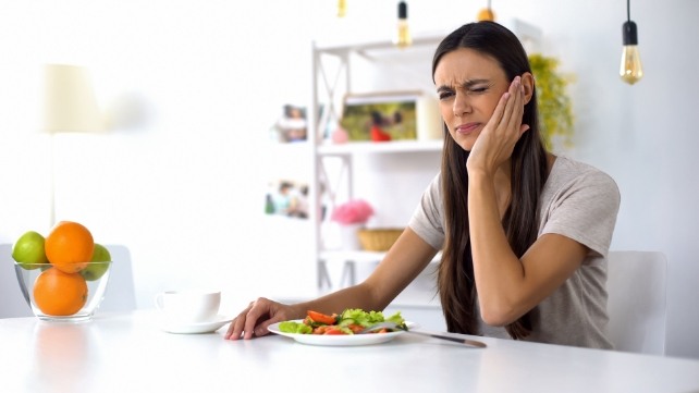 Woman at table with salad holding her cheek in pain