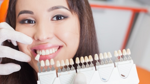 Smiling woman in dental chair next to color chart for veneers in Colchester