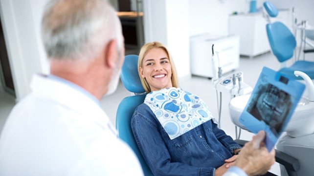 Dentist holding printout of digital X-Ray, speaking to happy patient