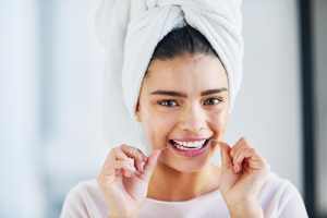 Woman with towel on head flossing teeth