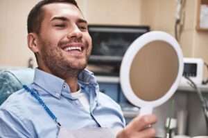 Happy dental patient looking at his teeth in mirror 